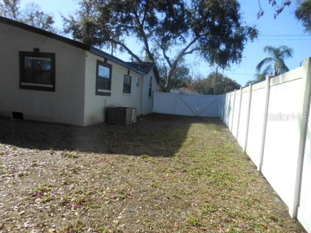 A side yard features a beige house, a white vinyl fence, and a gate — 8421 N ORANGEVIEW AVENUE, TAMPA, FL