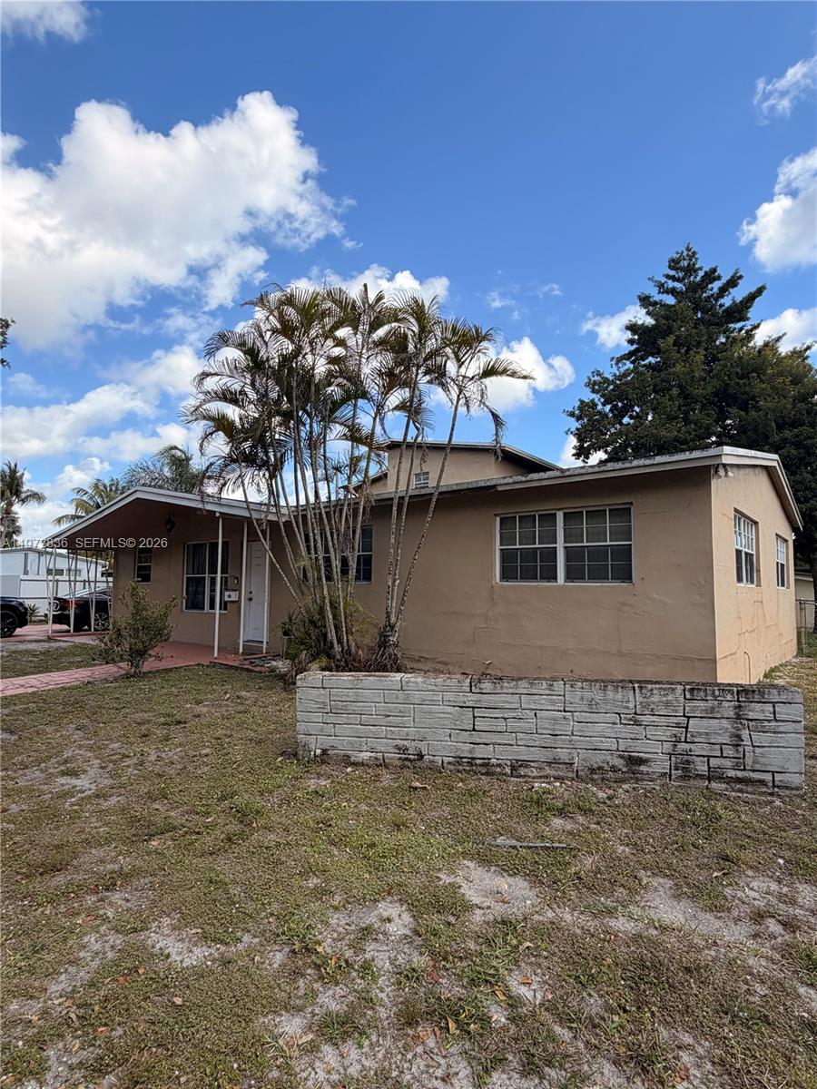 A single-story tan house with a palm tree in the front yard and a wall — 7191 Park St, Hollywood FL 33024, HOLLYWOOD, FL