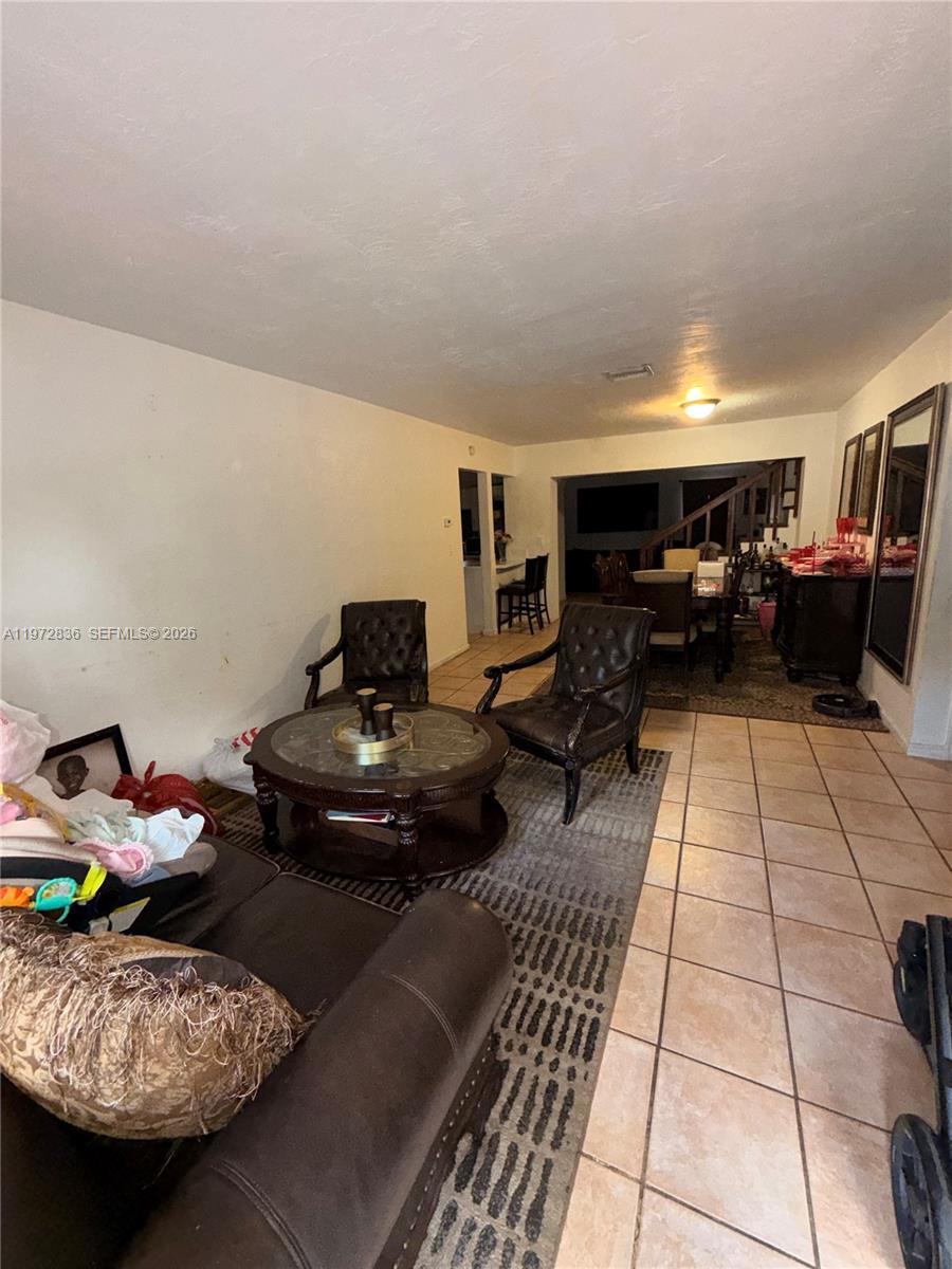 A living room with tile floors, a patterned rug, leather furniture, and an adjacent dining area — 7191 Park St, Hollywood FL 33024, HOLLYWOOD, FL