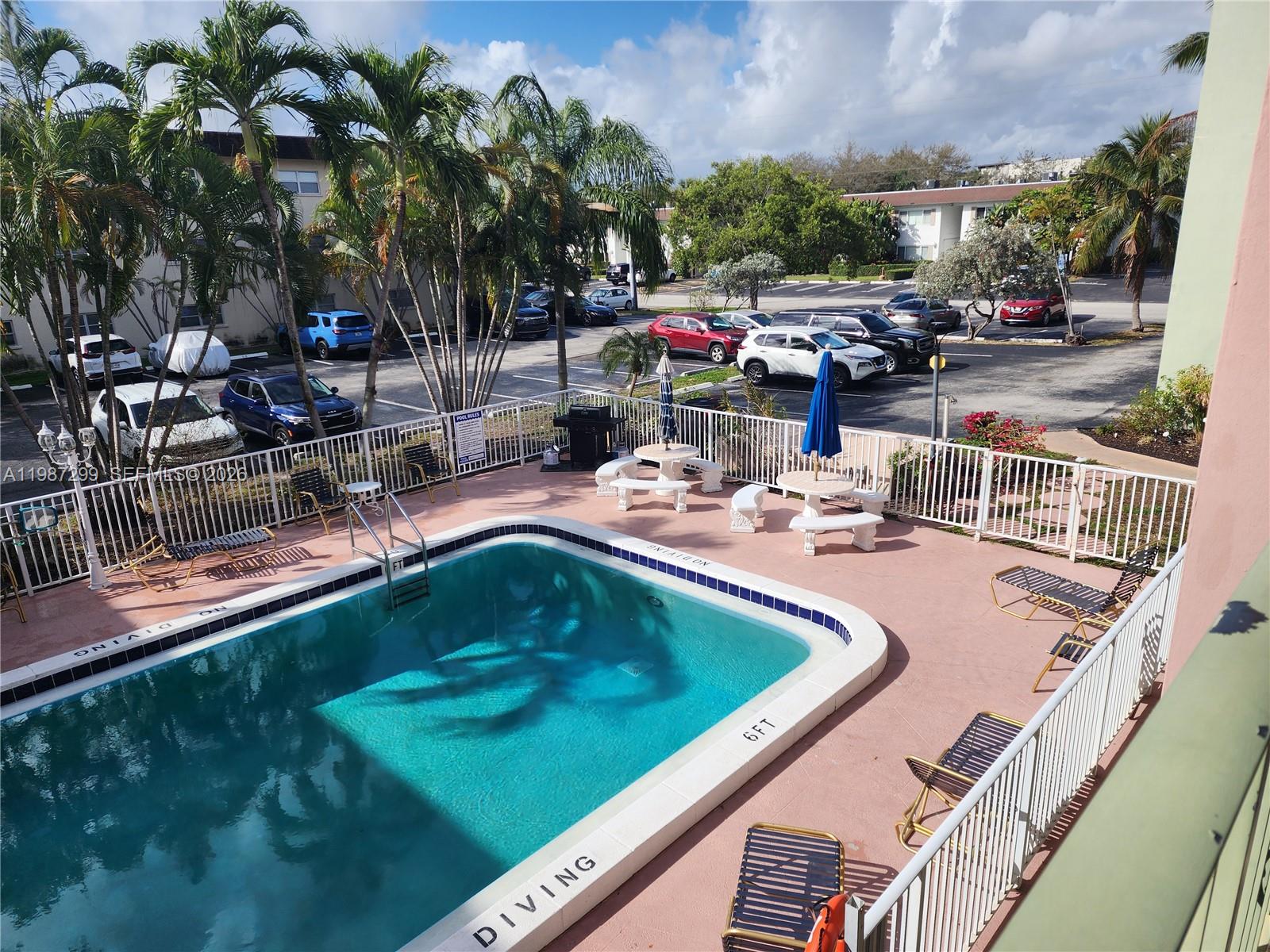 An elevated view of a swimming pool area with lounge chairs, tables, and a parking lot — 100 SE 6th Ave # 107, Pompano Beach FL 33060, POMPANO BEACH, FL