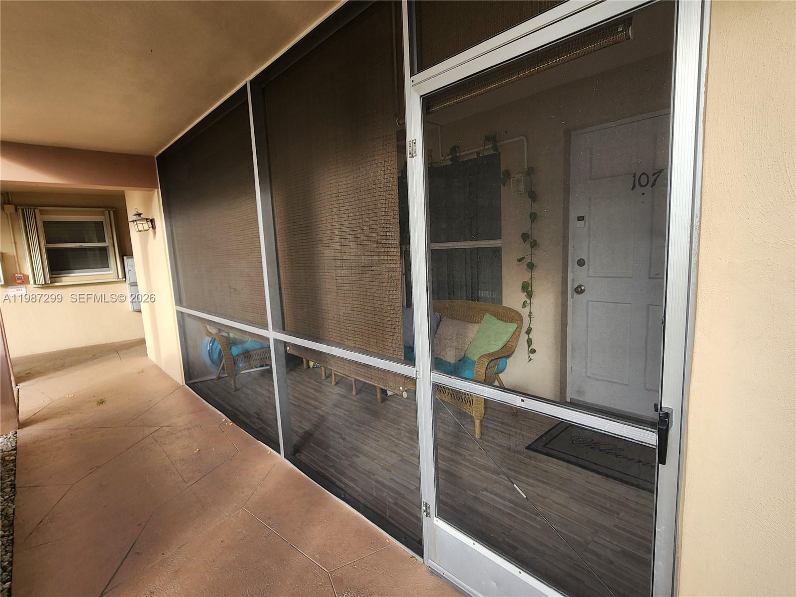 A screened-in porch features a wicker chair, wood-look flooring, and a white entry door — 100 SE 6th Ave # 107, Pompano Beach FL 33060, POMPANO BEACH, FL