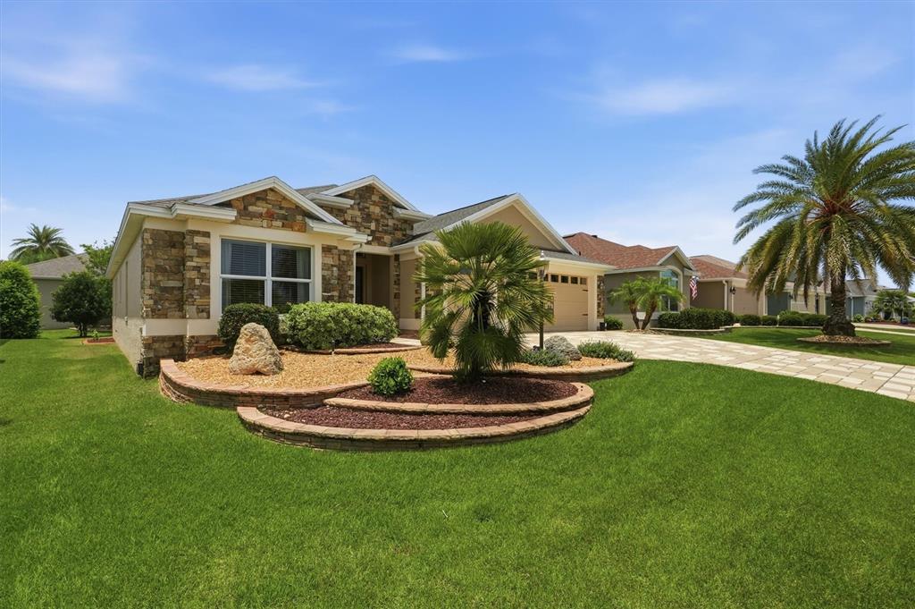 A single-story house with a stone facade, tiered landscaping, and a palm tree in front — 2938 ADRIENNE WAY, THE VILLAGES, FL