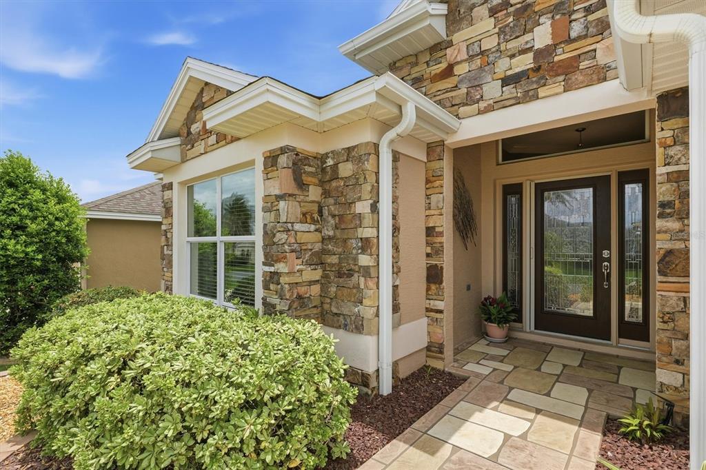 The exterior of a home features stone veneer, a covered entryway, and a glass-paneled door — 2938 ADRIENNE WAY, THE VILLAGES, FL