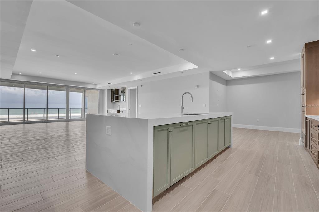 A modern kitchen island with sage green cabinets and white countertops sits in an open room — 70 AVENIDA VENECCIA UNIT 202, SARASOTA, FL