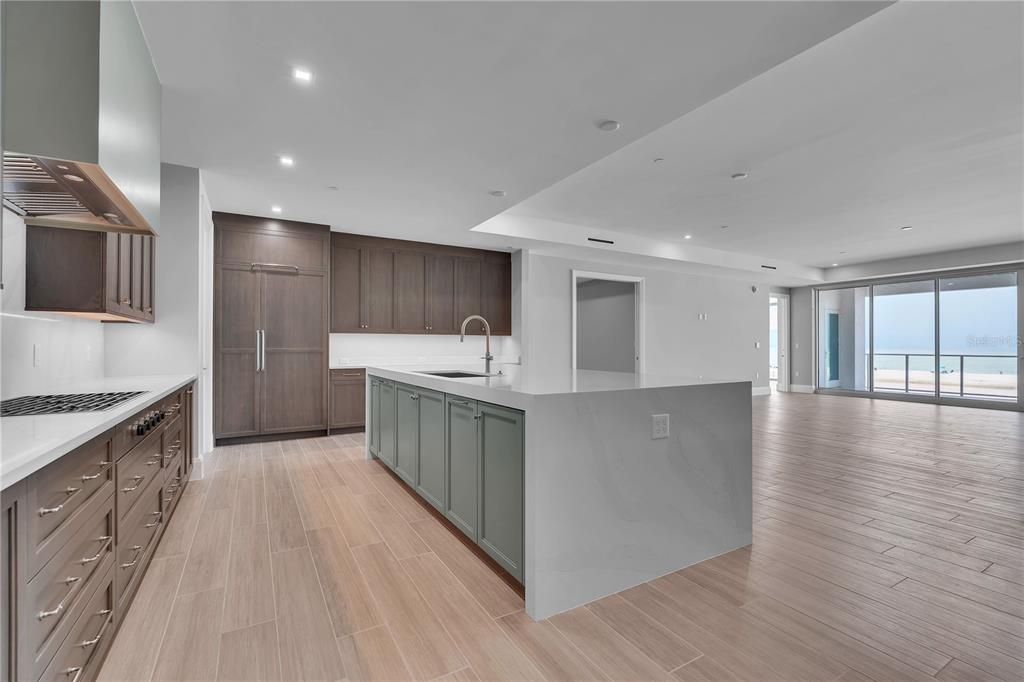 A modern kitchen features dark wood cabinetry, a sage green island, and light wood flooring — 70 AVENIDA VENECCIA UNIT 202, SARASOTA, FL