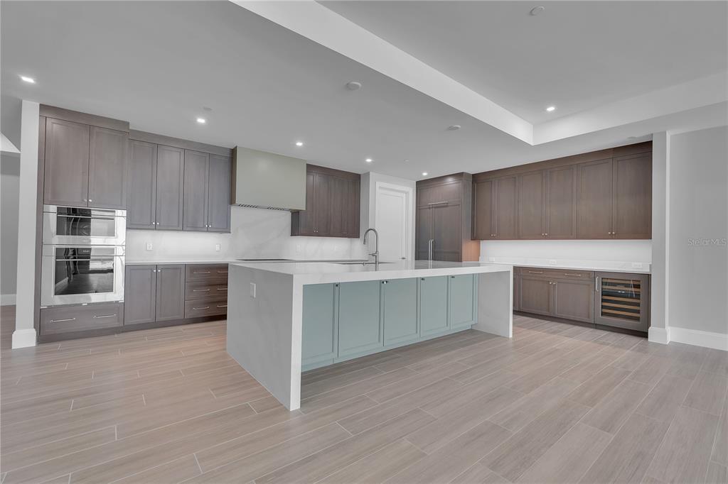 A modern kitchen features dark wood cabinetry, a light blue island, and white countertops — 70 AVENIDA VENECCIA UNIT 202, SARASOTA, FL