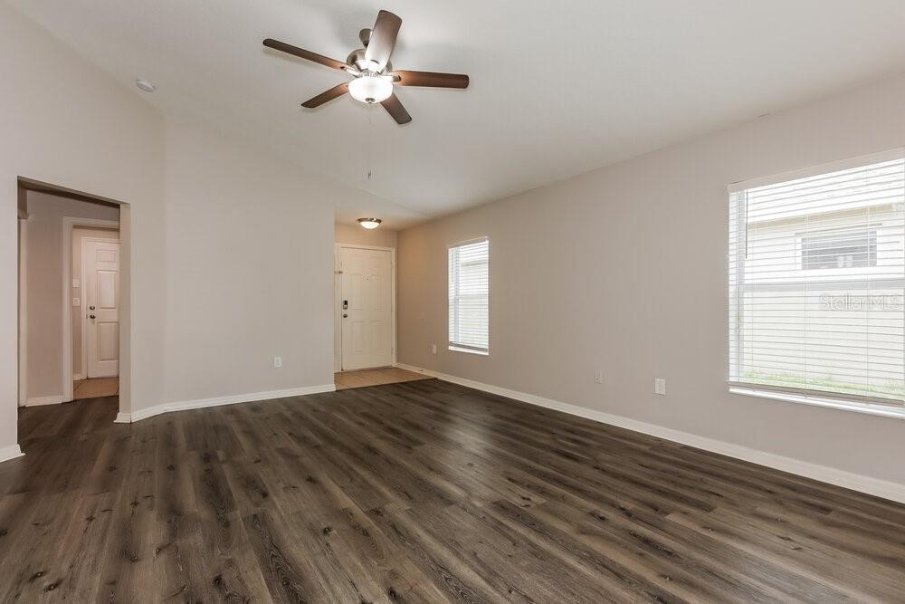An empty living room features wood-look flooring, a vaulted ceiling, and a ceiling fan — 10323 HOLLAND ROAD, RIVERVIEW, FL