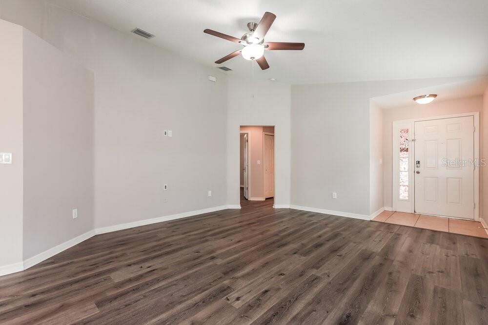 An empty living room features vaulted ceilings, a ceiling fan, and wood-look laminate flooring — 10323 HOLLAND ROAD, RIVERVIEW, FL