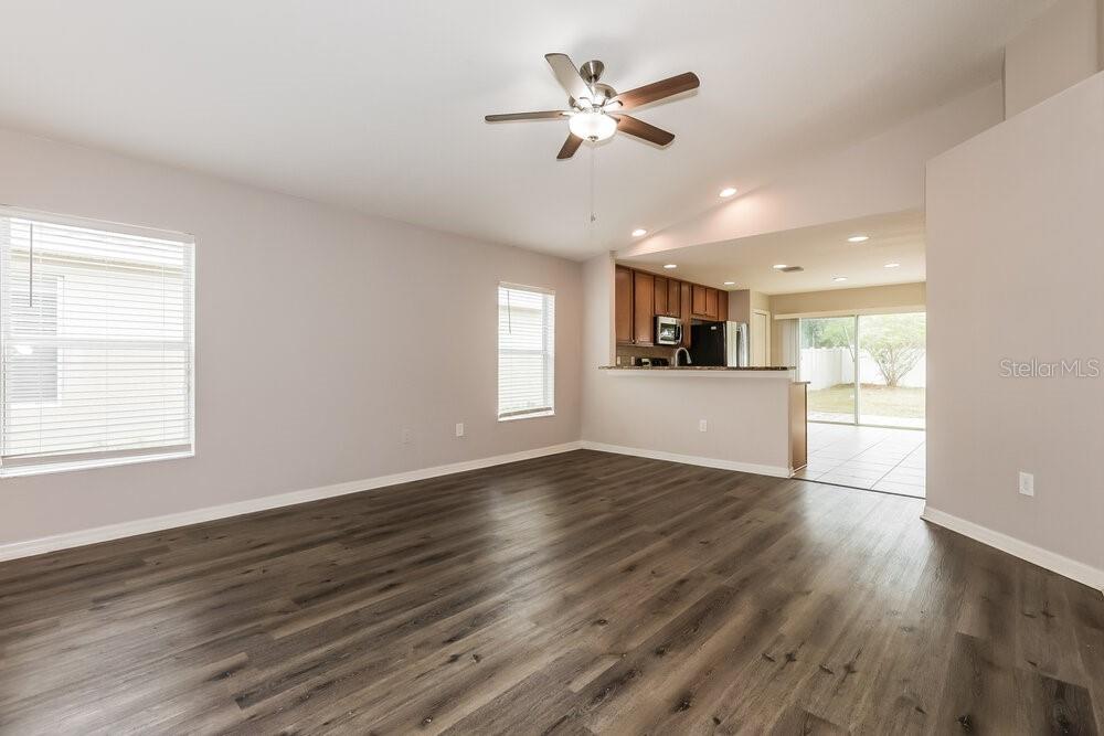 A living room with wood-look flooring, a ceiling fan, and an open kitchen beyond — 10323 HOLLAND ROAD, RIVERVIEW, FL