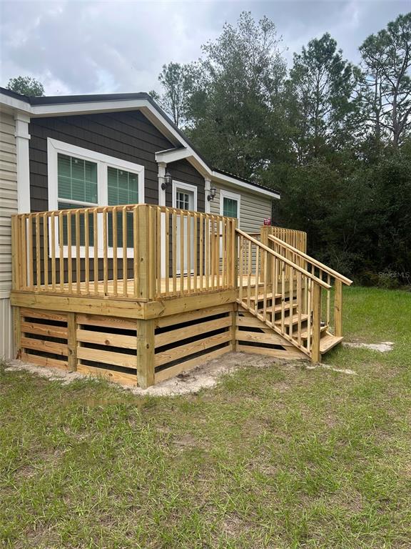 A wooden deck with railings and stairs sits in front of a house with siding — 10865 NE 220TH STREET, FORT MC COY, FL