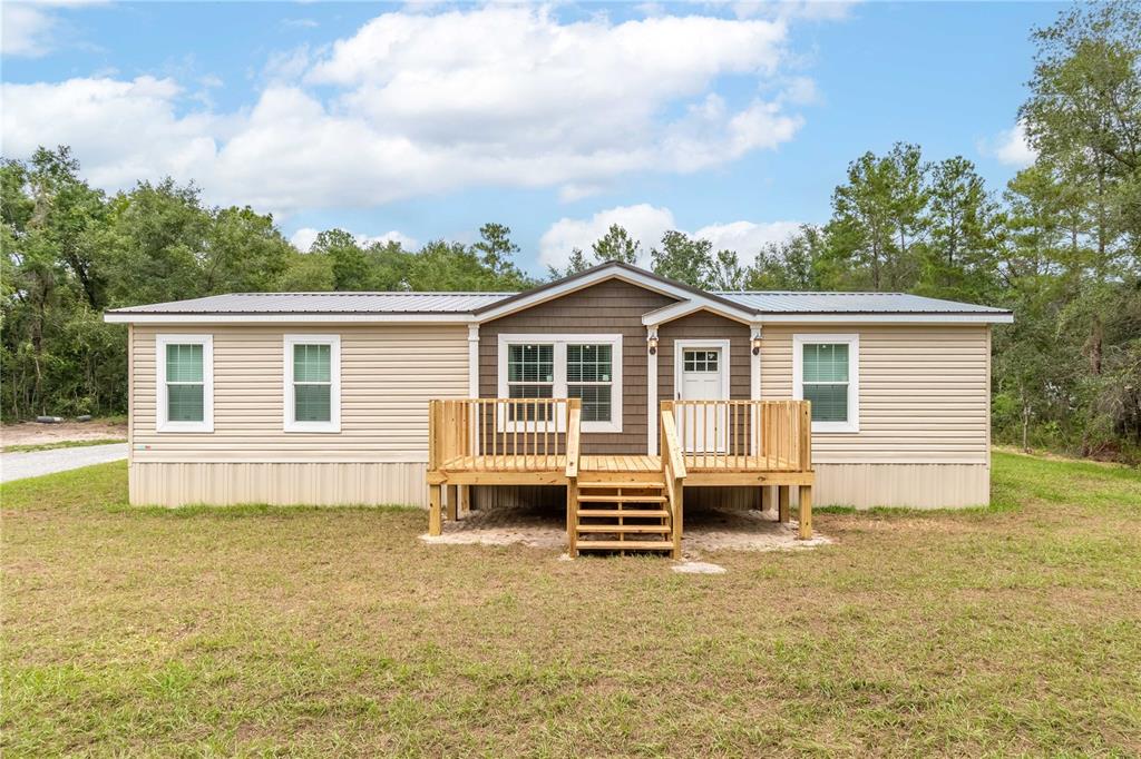 A single-story manufactured home with tan siding, a brown accent gable, and a wooden deck — 10865 NE 220TH STREET, FORT MC COY, FL
