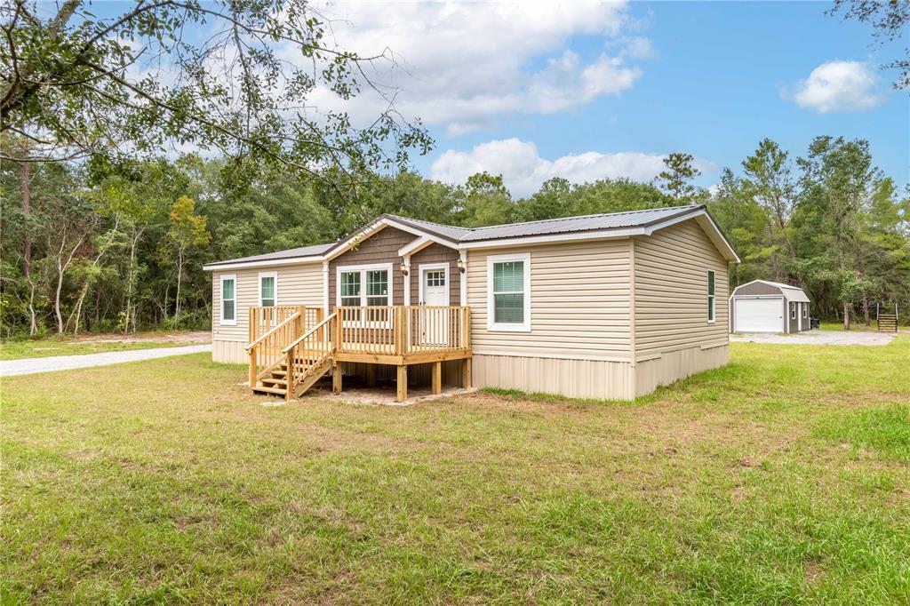 A tan manufactured home with a wooden deck and a detached garage in a yard — 10865 NE 220TH STREET, FORT MC COY, FL