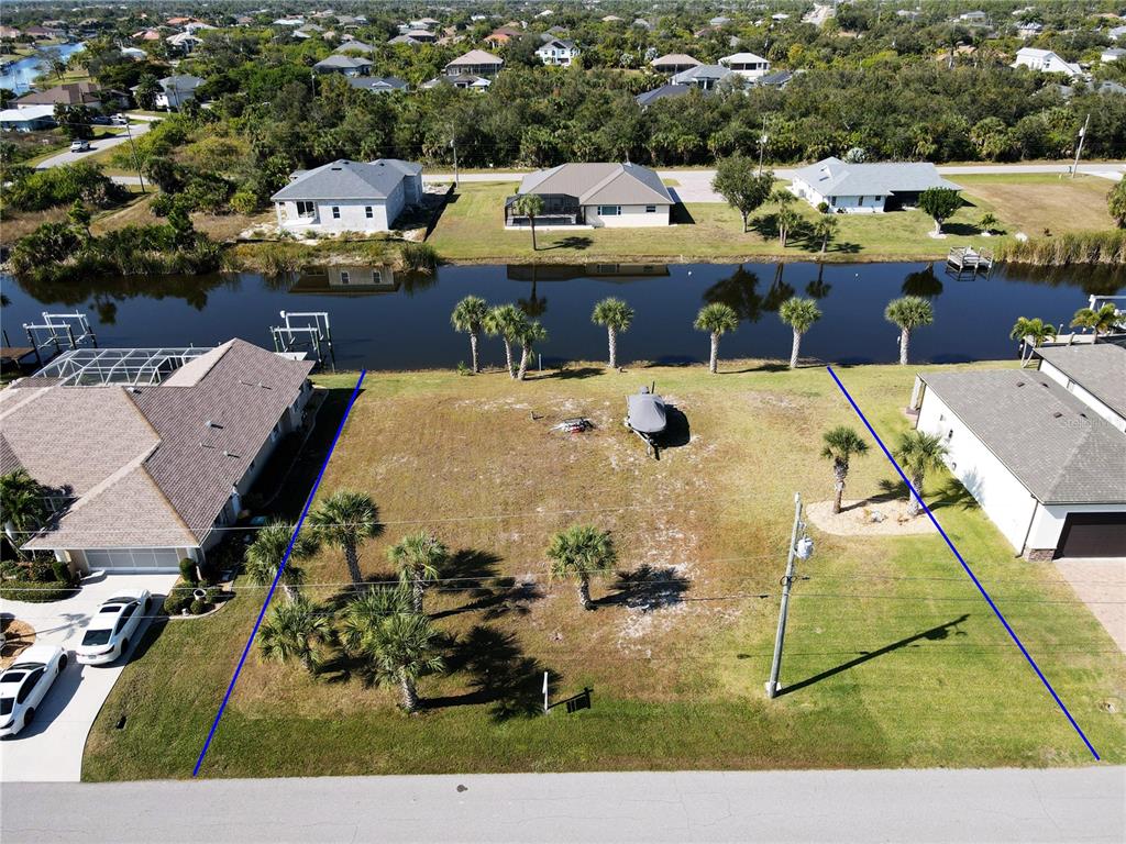 An aerial view shows a vacant waterfront residential lot outlined in blue between two houses — 9514 SNAPPER CIRCLE, PORT CHARLOTTE, FL