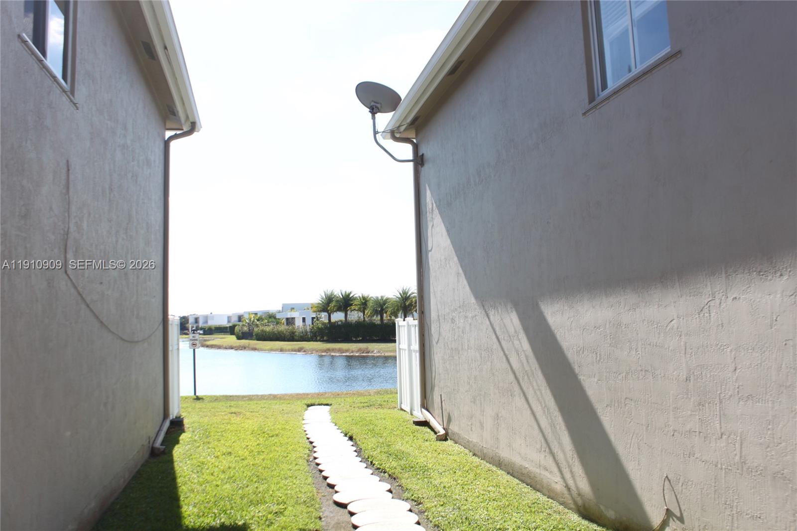 A grassy path leads between two beige houses toward a lake and palm trees — 180 Riviera Cir # 5, Weston FL 33326, WESTON, FL