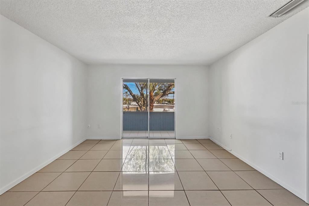 An empty room with beige tile flooring, white walls, and sliding glass doors to a balcony — 5503 FOUNTAIN LAKE CIRCLE UNIT A204, BRADENTON, FL