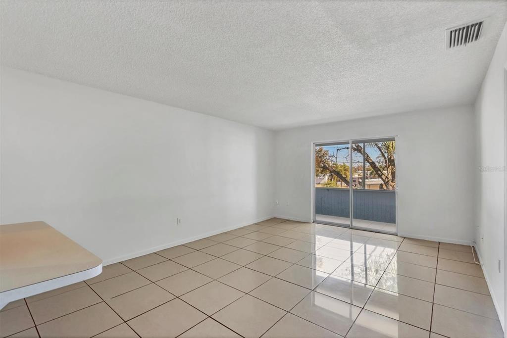 An empty room with white walls, beige tile flooring, and a sliding glass balcony door — 5503 FOUNTAIN LAKE CIRCLE UNIT A204, BRADENTON, FL