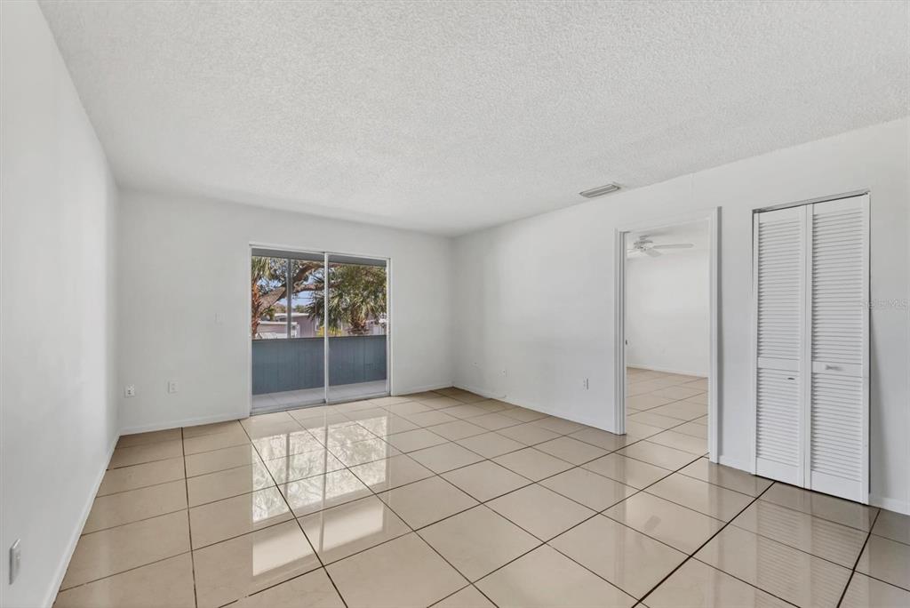 An empty room with beige tile flooring, white walls, a sliding glass door, and closet — 5503 FOUNTAIN LAKE CIRCLE UNIT A204, BRADENTON, FL