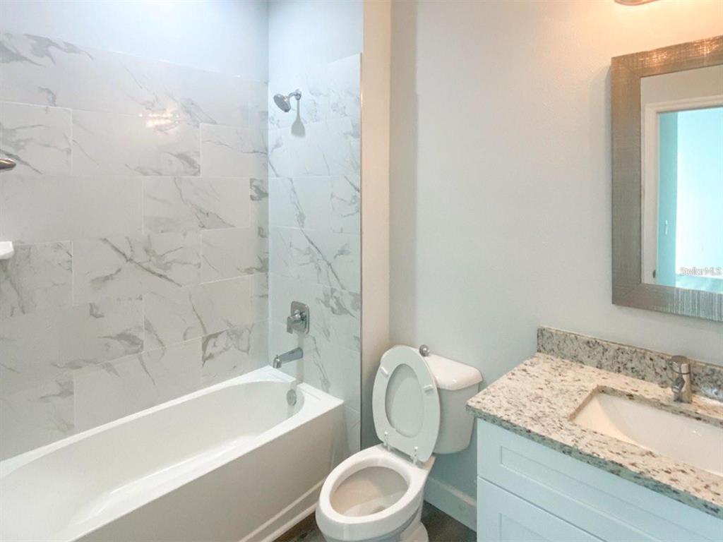 A bathroom features a white bathtub with marble-look tile, a toilet, and a granite vanity — 8519 AGATE STREET UNIT 8521, PORT CHARLOTTE, FL