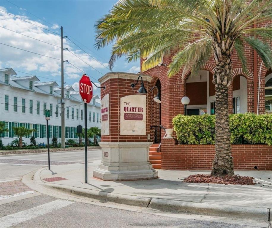 A brick monument sign for The Quarter Condominium Association stands on a sidewalk near palm trees — 1880 E PALM AVENUE, TAMPA, FL