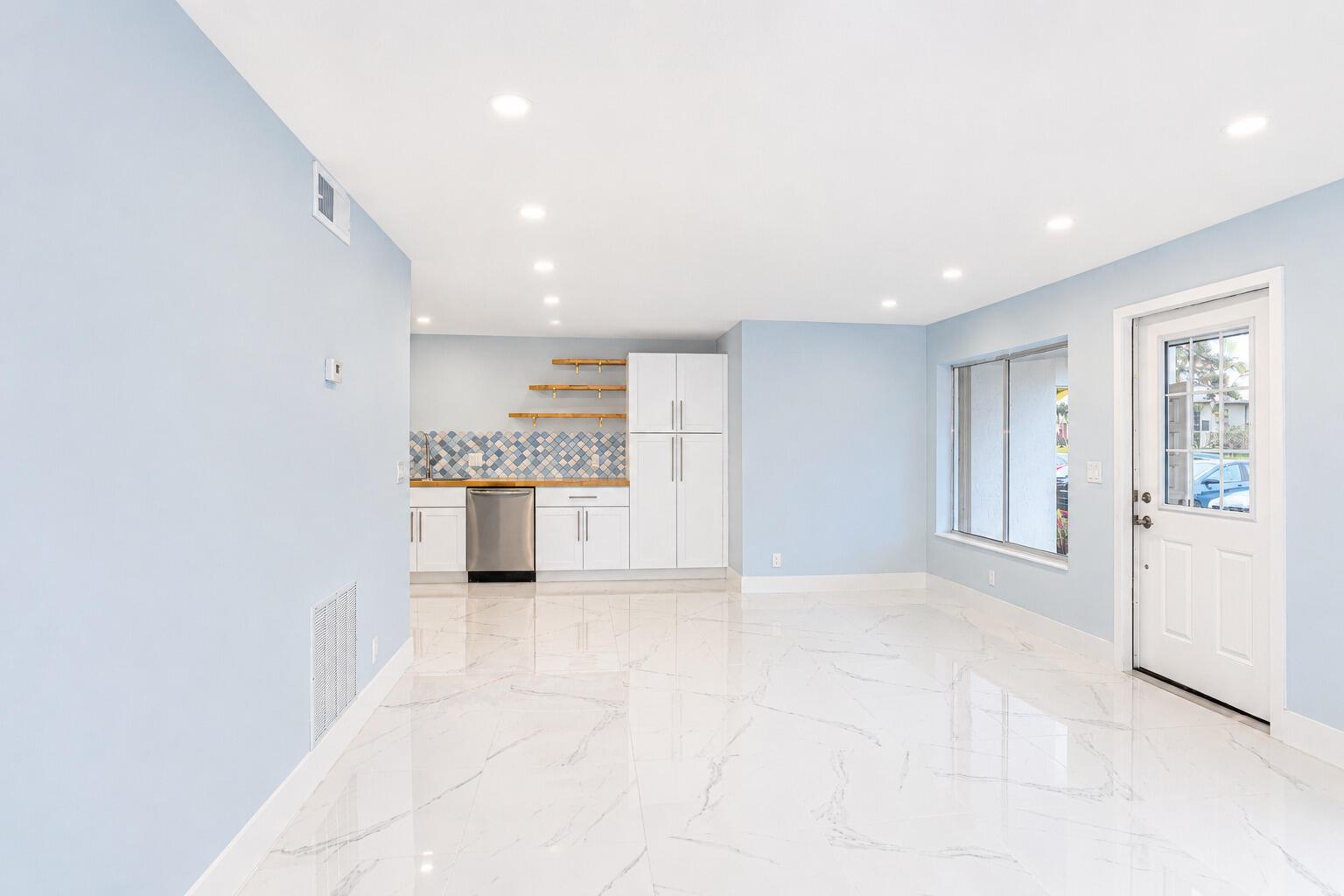 A bright room with light blue walls, white tile flooring, and a small kitchen area — 303 Knotty Pine Circle # 1, FL 33463, FL