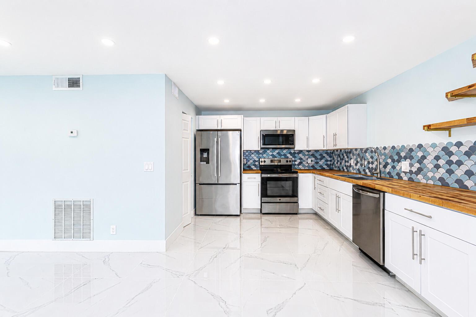 A kitchen with white cabinets, stainless steel appliances, wood countertops, and a blue scalloped backsplash — 303 Knotty Pine Circle # 1, FL 33463, FL