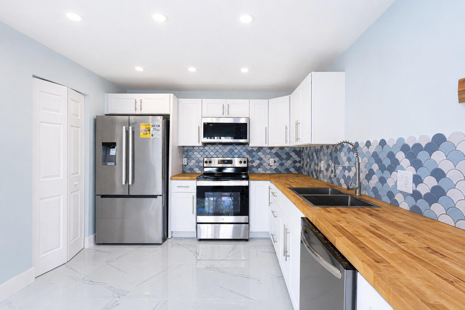 A kitchen with white cabinets, wood countertops, stainless steel appliances, and blue scalloped tile backsplash — 303 Knotty Pine Circle # 1, FL 33463, FL