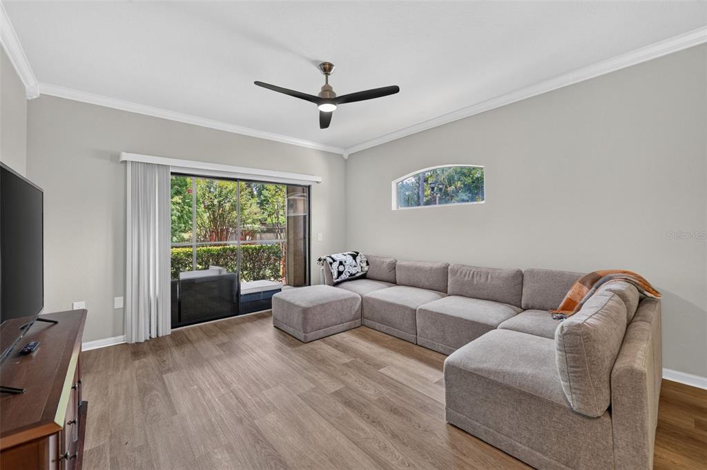 A living room features light wood-look flooring, a sectional sofa, a television console, and sliding doors — 2217 TUSCANY TRACE UNIT 7, PALM HARBOR, FL