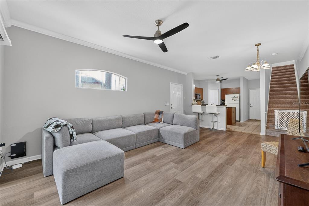 A living room features a grey sectional sofa, wood-look flooring, a ceiling fan, and sliding doors — 2217 TUSCANY TRACE UNIT 7, PALM HARBOR, FL