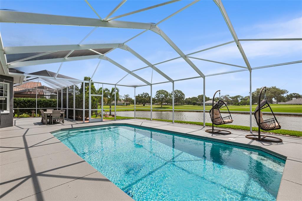 A screened-in pool patio overlooks a lake and golf course with outdoor seating — 4040 PALMA CEIA CIRCLE, WINTER HAVEN, FL