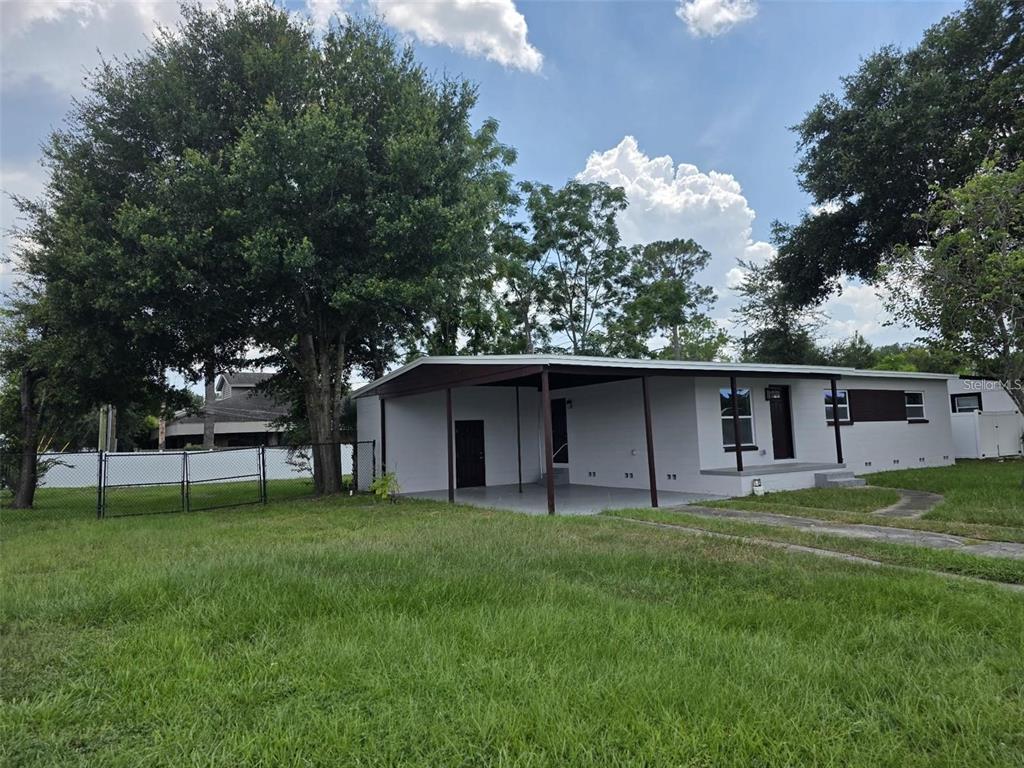 A single-story house with a carport, gray exterior, and a large front yard with trees — 5660 PECOS STREET, ORLANDO, FL