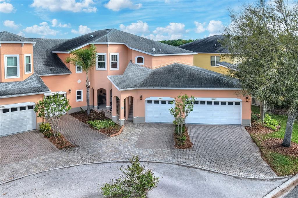 An exterior view of a multi-unit peach-colored house with three garage doors and pavers — 3933 SERENADE LANE, LAKELAND, FL