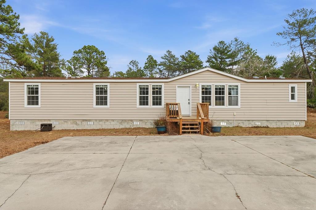A single-story manufactured home with beige siding and a concrete driveway sits among trees — 7545 N DAMASCUS AVENUE, DUNNELLON, FL