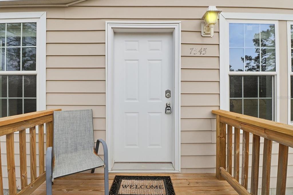A white front door with a welcome mat sits on a wooden porch — 7545 N DAMASCUS AVENUE, DUNNELLON, FL