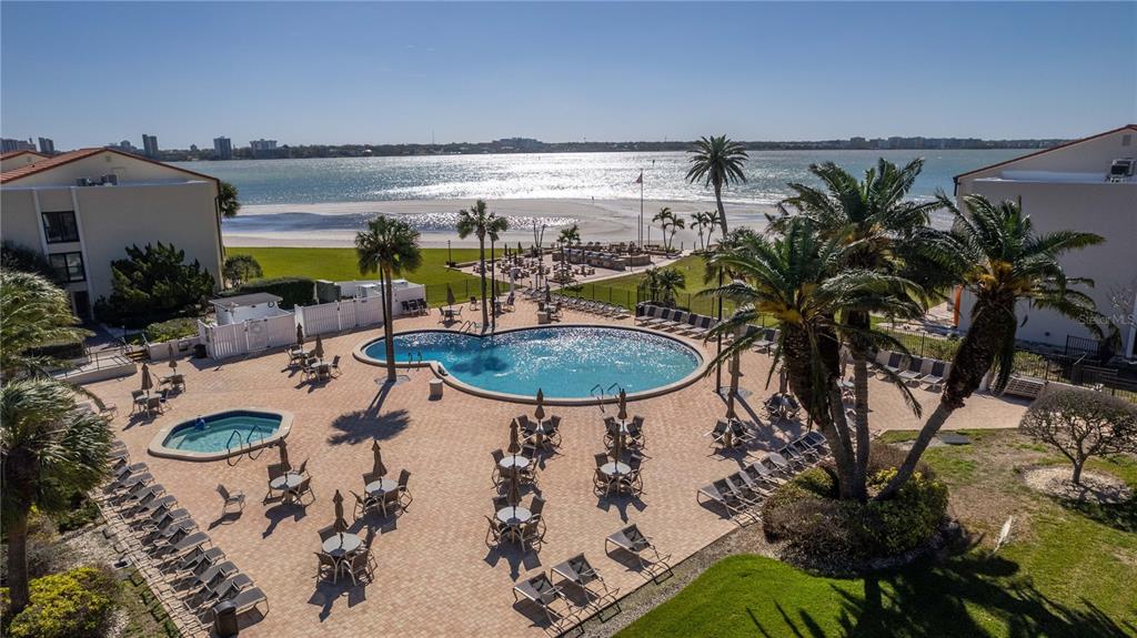 An aerial view shows a swimming pool and patio area overlooking a beach and ocean — 830 S GULFVIEW BOULEVARD UNIT 501, CLEARWATER BEACH, FL