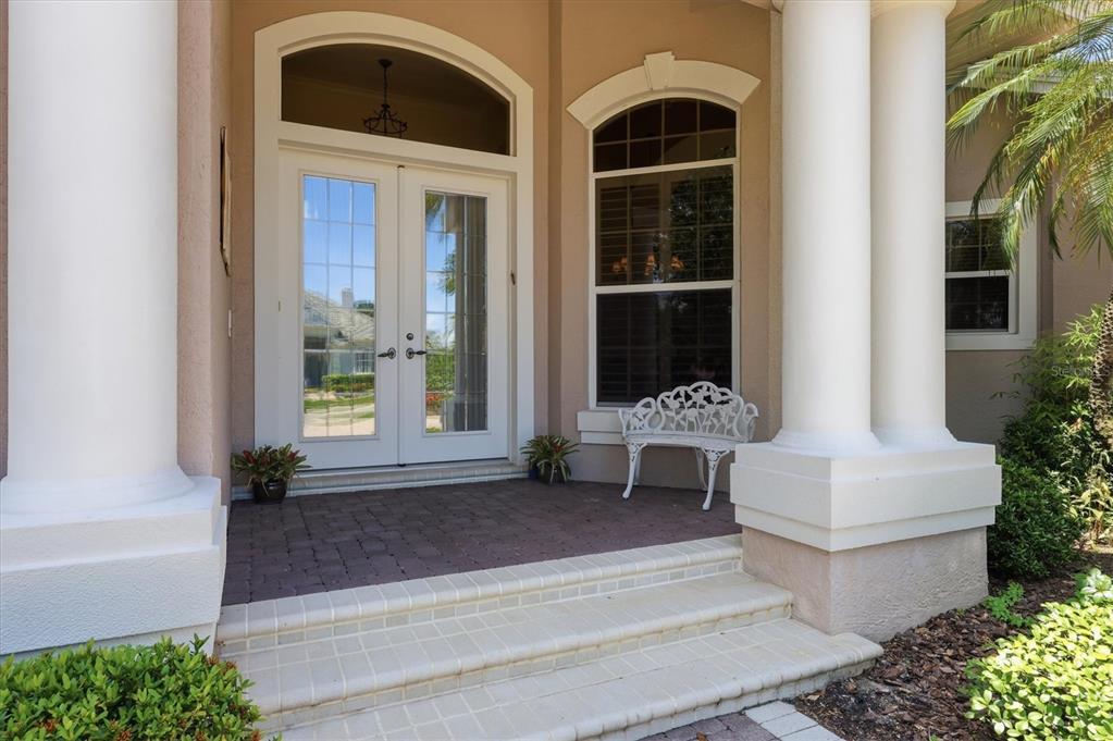 A covered front porch features double glass doors, white columns, and a small white bench — 7218 MARLOW PLACE, UNIVERSITY PARK, FL