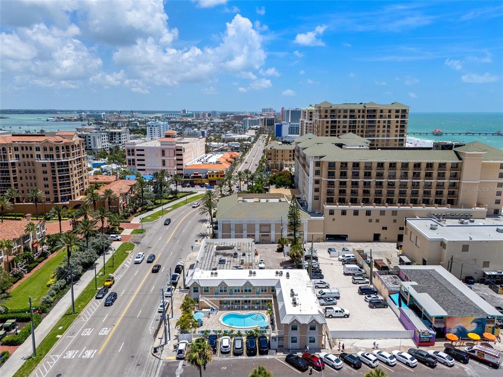 An aerial view shows a coastal street with hotels, a swimming pool, and parking lots — 530 MANDALAY AVENUE UNIT 106, CLEARWATER BEACH, FL
