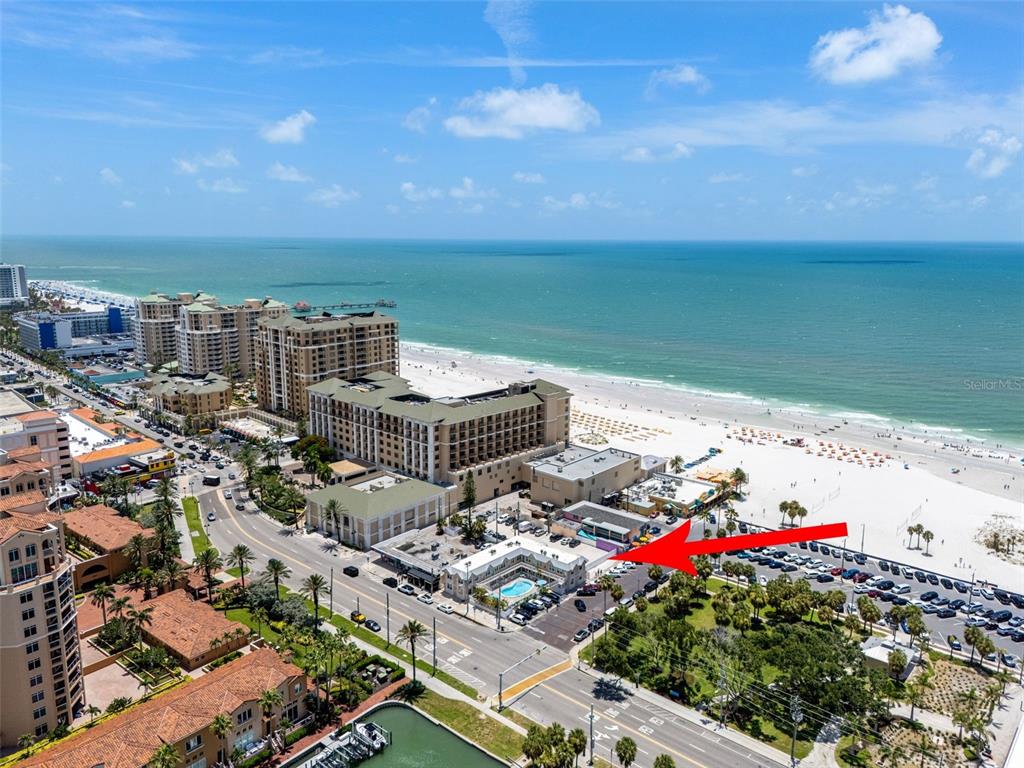 An aerial view shows a beachside hotel with a pool, parking lot, and oceanfront access — 530 MANDALAY AVENUE UNIT 106, CLEARWATER BEACH, FL