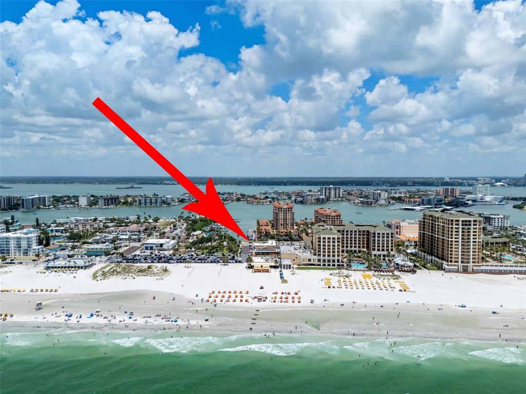 An aerial view of a beach resort area with a red arrow pointing toward buildings — 530 MANDALAY AVENUE UNIT 106, CLEARWATER BEACH, FL