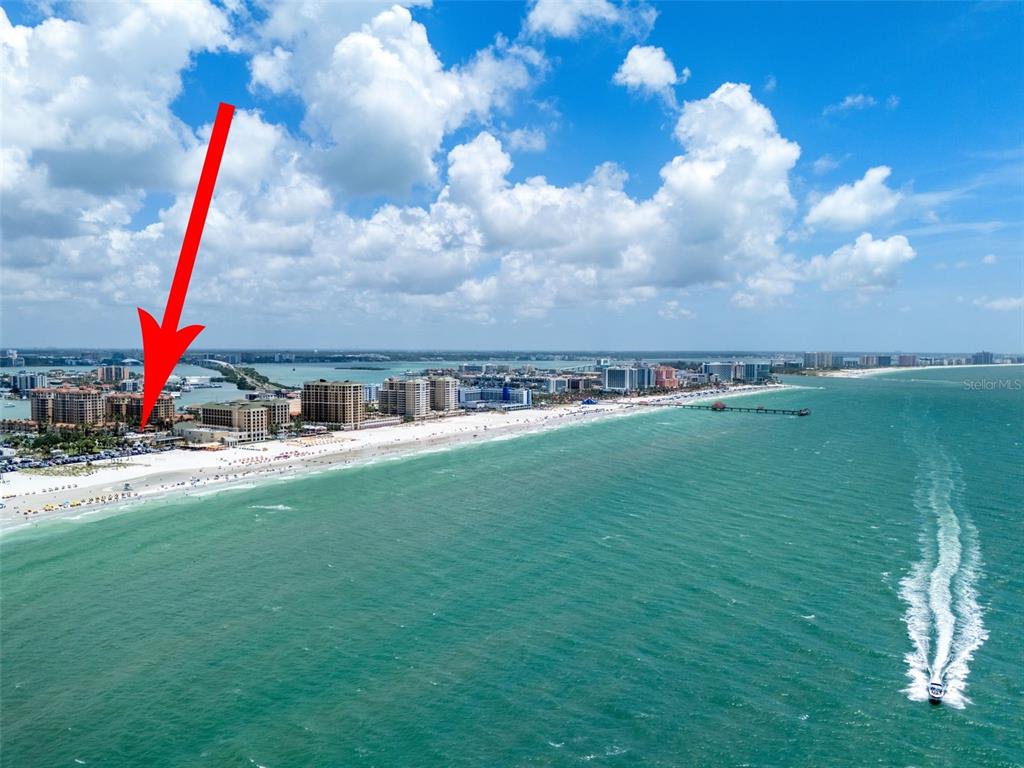 An aerial view shows a beach resort with a red arrow pointing toward the buildings — 530 MANDALAY AVENUE UNIT 106, CLEARWATER BEACH, FL