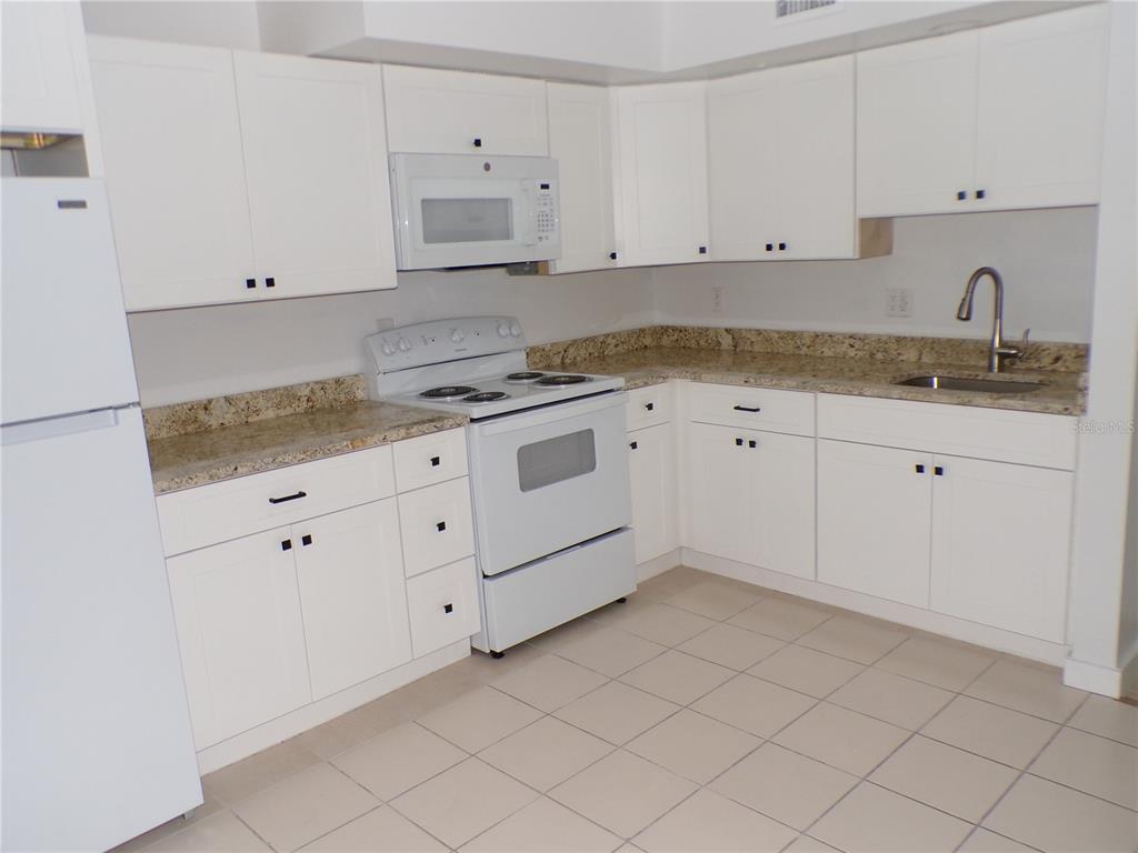A kitchen features white cabinets, granite countertops, white appliances, and light-colored tile flooring — 1258 BARBARA DRIVE UNIT 106, VENICE, FL