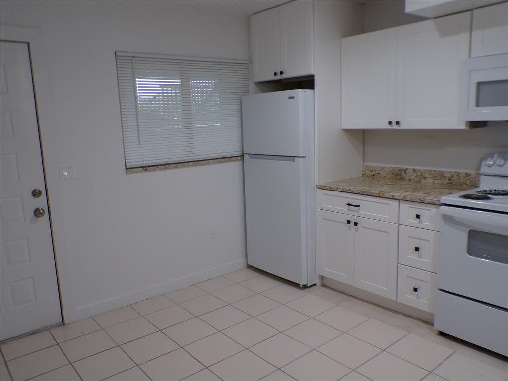 A kitchen features white cabinets, a white refrigerator, a white stove, and tiled flooring — 1258 BARBARA DRIVE UNIT 106, VENICE, FL