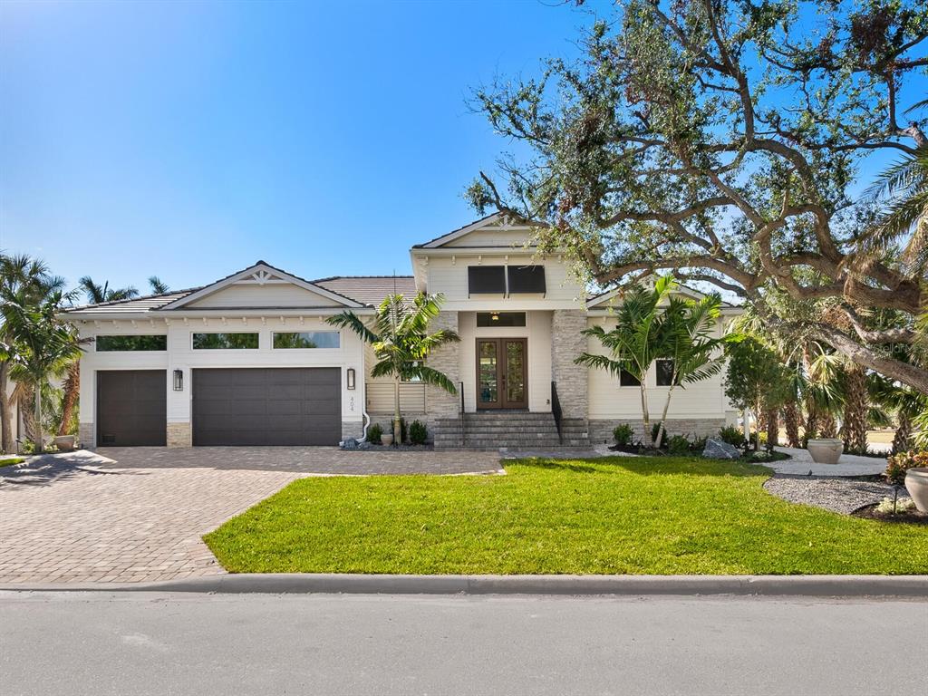 A single-story house with a paved driveway, three-car garage, and stone accents under a clear sky — 482 E ROYAL FLAMINGO DRIVE, SARASOTA, FL