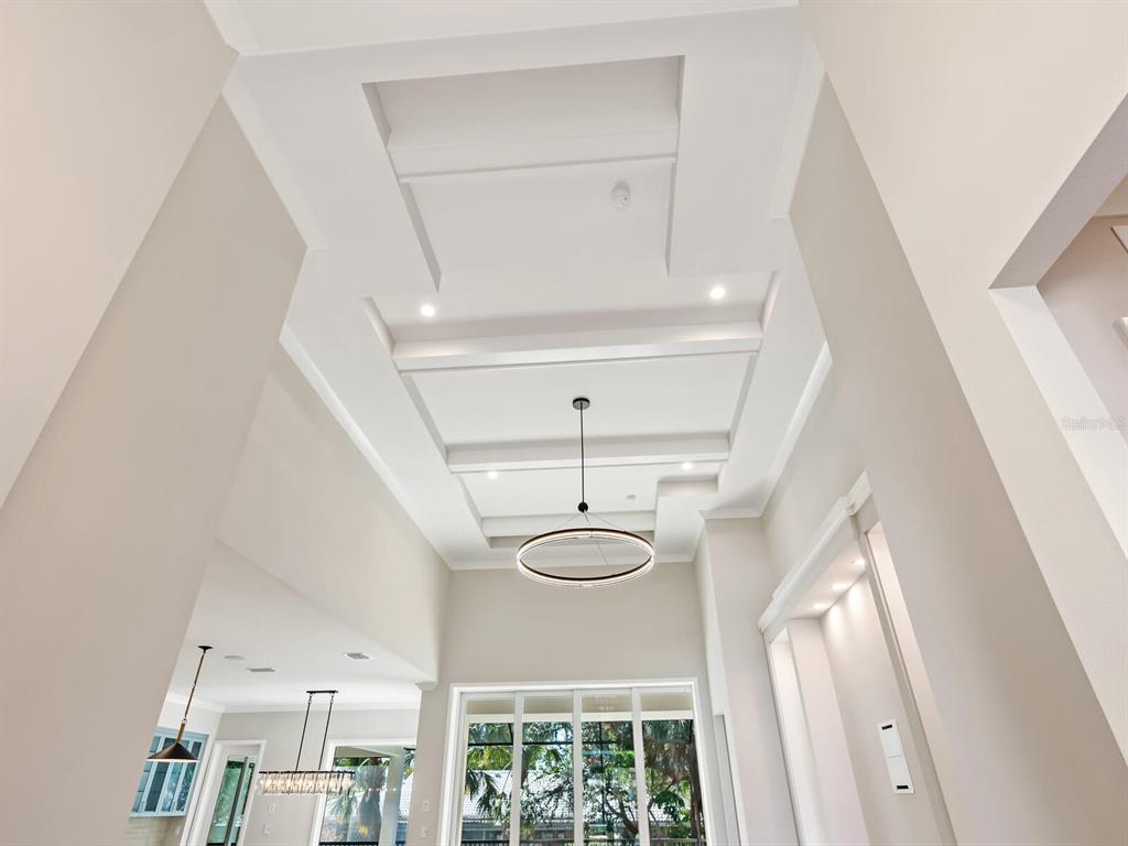 A high-ceilinged room features a tiered tray ceiling, a modern ring chandelier, and recessed lighting — 482 E ROYAL FLAMINGO DRIVE, SARASOTA, FL