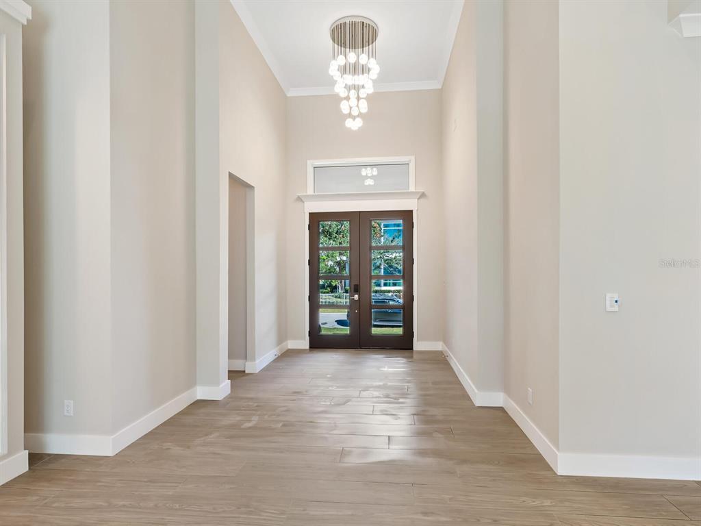A high-ceilinged entryway features wood-look tile flooring, a modern chandelier, and dark-framed glass doors — 482 E ROYAL FLAMINGO DRIVE, SARASOTA, FL