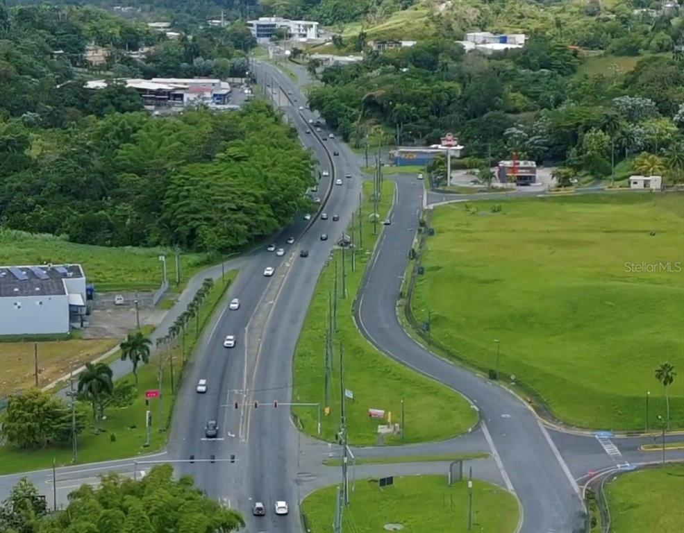 An aerial view shows a multi-lane highway curving through a lush, green landscape — Carretera 1 BARRIO QUEBRADA ARENA, SAN JUAN, PR