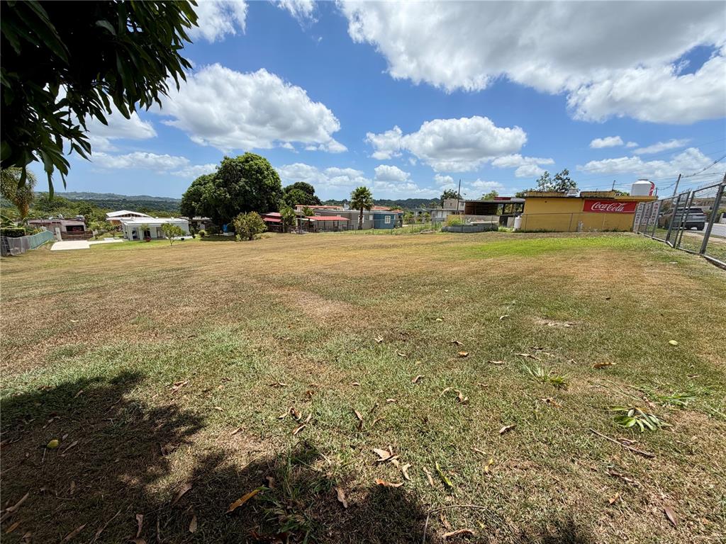 A large, grassy, open lot features a yellow building with a Coca-Cola sign nearby — CARR 662, MOROVIS, PR