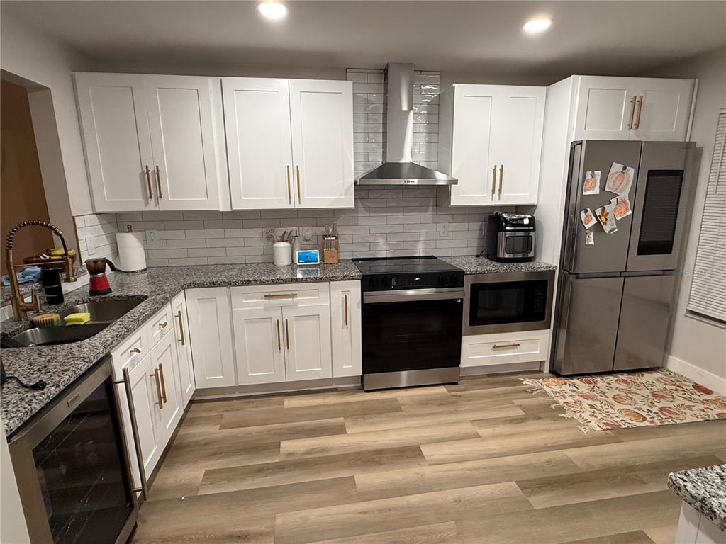 A kitchen features white cabinets, granite countertops, stainless steel appliances, and wood-look flooring — 11165 EINBENDER ROAD, ORLANDO, FL