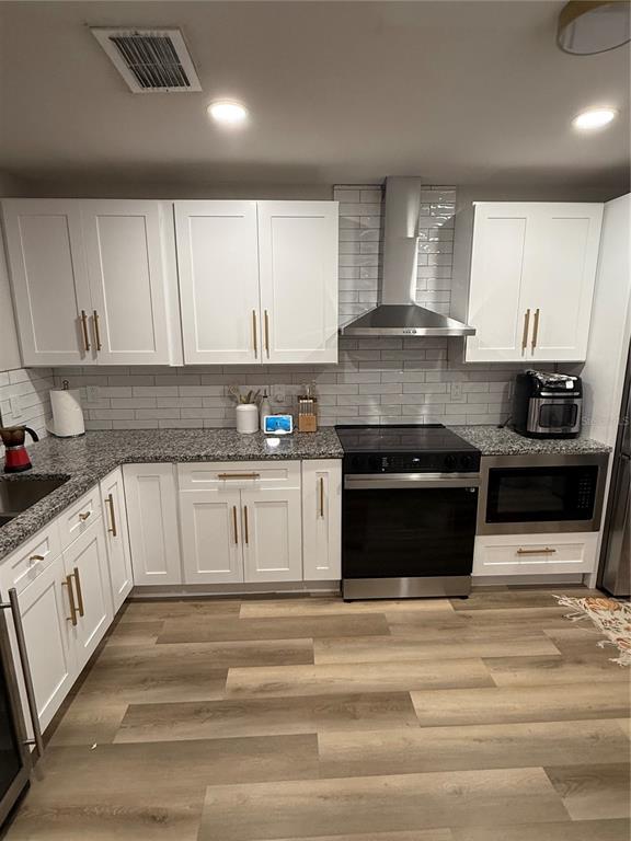A kitchen features white cabinets, granite countertops, stainless steel appliances, and light wood-look flooring — 11165 EINBENDER ROAD, ORLANDO, FL