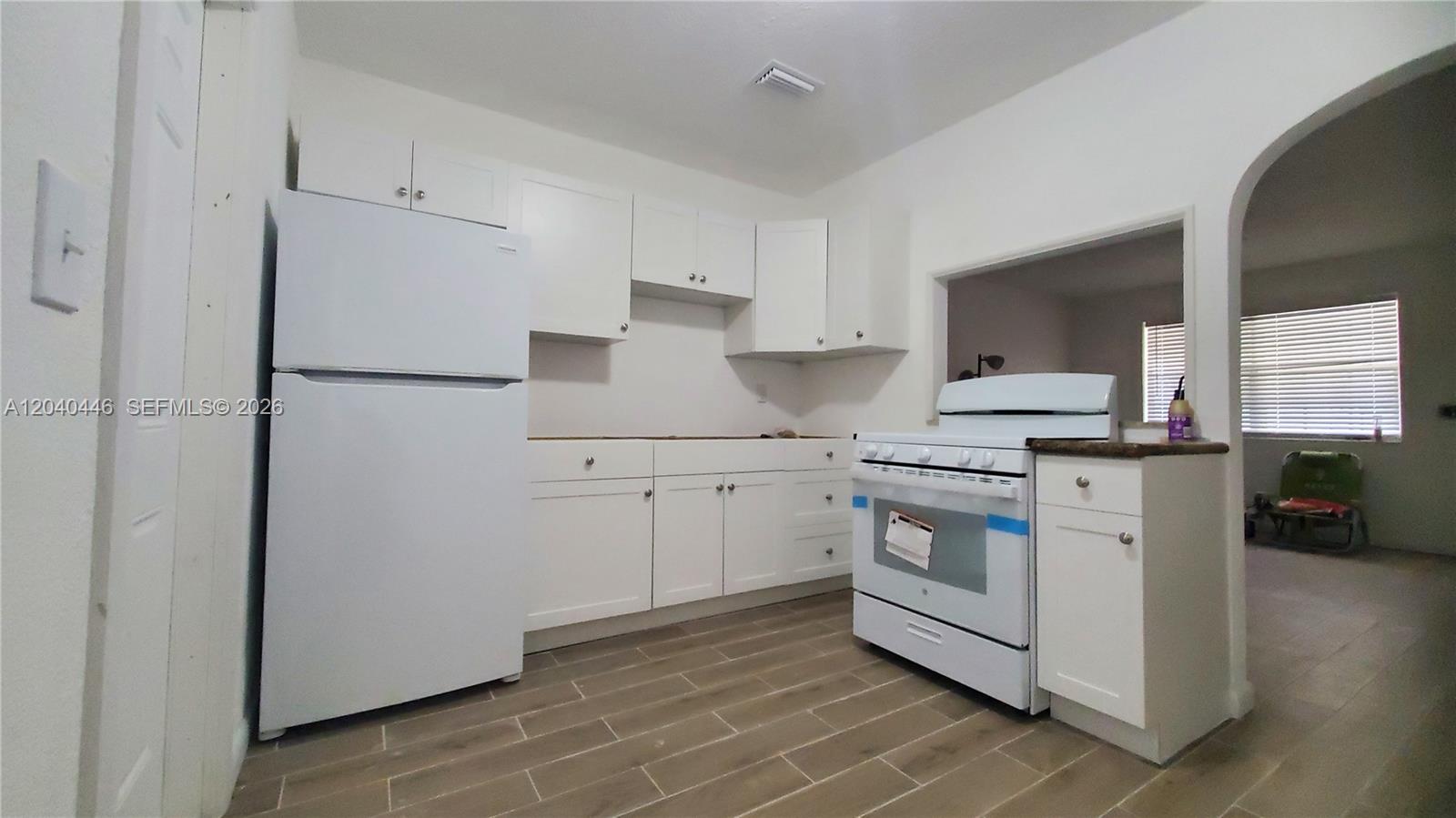 A kitchen features white cabinets, white appliances, and wood-look tile flooring — 905 SW 4th Ter, Hallandale Beach FL 33009, HALLANDALE BEACH, FL