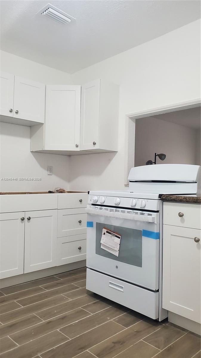 A kitchen features white cabinets, a new white stove, and wood-look tile flooring — 905 SW 4th Ter, Hallandale Beach FL 33009, HALLANDALE BEACH, FL